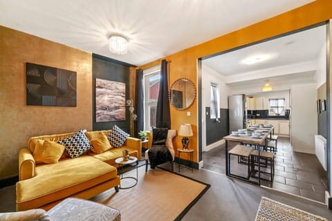 Open-plan living area with a yellow sofa, coffee table, and dining space leading through to the kitchen.
