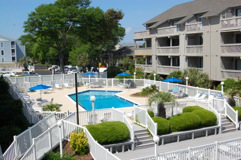 Beautiful resort pool area with white railings, lounge chairs, and landscaping surrounded by vacation rental buildings.