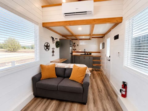 Cozy living room featuring a loveseat, electric fireplace, Smart TV, and open kitchen layout. Large windows provide natural light and outdoor views, creating a bright and comfortable gathering space for couples, families, or friends.