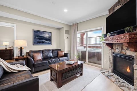 Warm and inviting living room with a stone fireplace, leather seating, and sliding doors leading to a private balcony with mountain views.