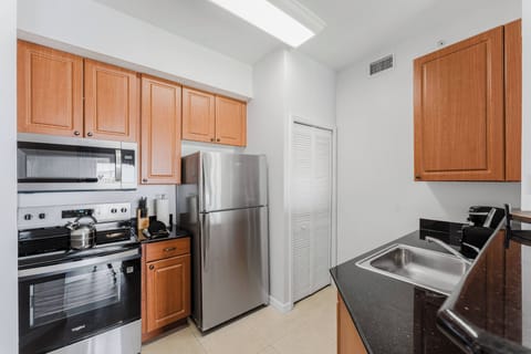 Enjoy a functional kitchen with rich wooden cabinets and sleek black countertops, complemented by stainless steel appliances. Bright lighting creates an inviting atmosphere, perfect for preparing delicious meals during your visit.
