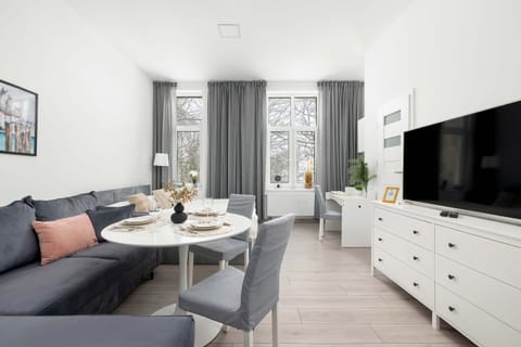 A bright living room with a sofa, a round coffee table, and a 43-inch TV on a white stand. Natural light fills the space, creating a cozy atmosphere.