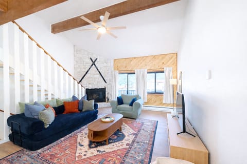 Sunny vaulted living room with stone fireplace, beams, and views.
