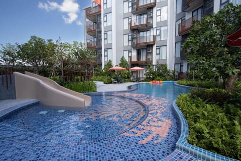 Large outdoor pool with a water slide, surrounded by greenery and modern residential buildings.