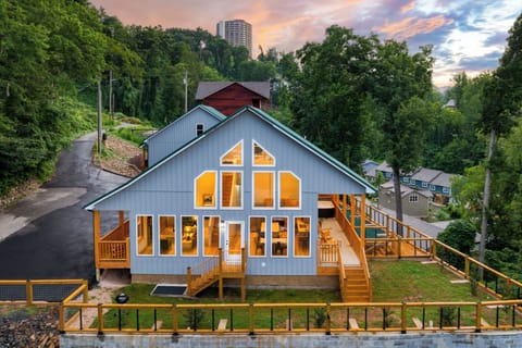 Warm sunset glow over this modern mountain home, featuring expansive windows, wraparound decks, and a peaceful wooded hillside setting. (Perfect Too)