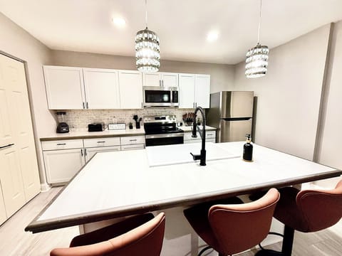 Large island with farmhouse sink, quartz-style counters, and seating for gathering. Bright pendant lighting makes this the heart of the home for meals, games, and conversation.