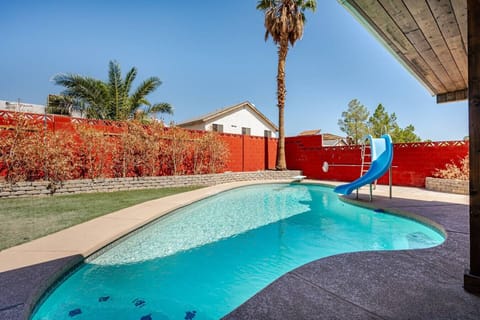 Beautiful backyard swimming pool with water slide, surrounded by palm trees - perfect for relaxation and fun in the sun.