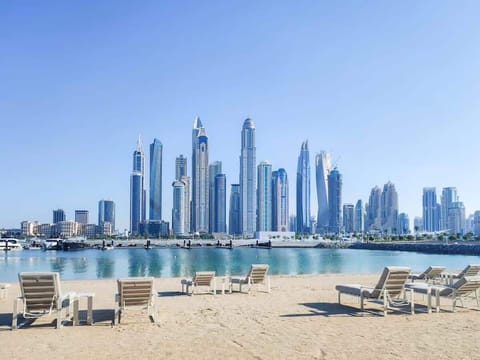 Scenic Private marina beach view with palm trees, sun loungers, and a vibrant city skyline in the background.