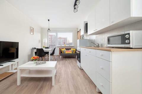 A view of the living room and kitchen from a different perspective. The white coffee table and TV area are visible, creating a comfortable lounging zone. The open layout connects all areas seamlessly.