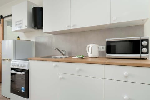 A compact kitchen scene with white cabinets, a stove, oven, and microwave. Wooden countertops soften the modern look. Everything appears clean and neatly arranged.