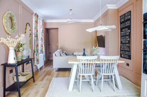 Bright interiors with soft tones, wooden dining table, and spindle‑back chairs under a sleek pendant light. A cozy sofa, decorative mirrors, and bold wall art add character. Designed for comfort.