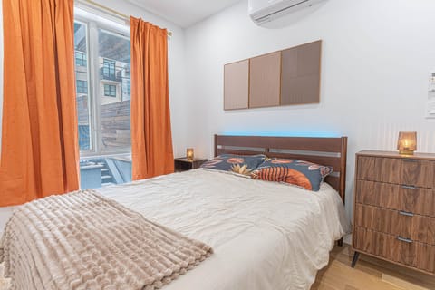 Wooden bed with blue LED light, floral pillows, orange curtains, a dresser, and wall panels.