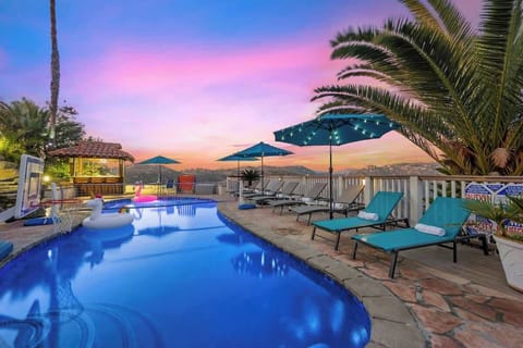 Stunning poolside retreat at sunset, featuring lounge chairs, umbrellas, and a breathtaking view of the lake and hills.