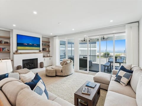 The cozy living room, adorned with plush seating and a sleek fireplace, offers breathtaking ocean views through expansive sliding doors, inviting relaxation and coastal charm.