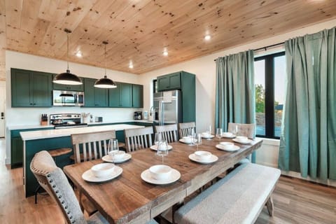 Gather around your rustic dining table under warm wood ceilings, where green cabinetry and modern appliances create the perfect space for memorable meals.