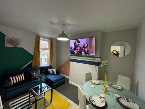 A living and dining area with a sofa, wall-mounted TV, and set dining table.