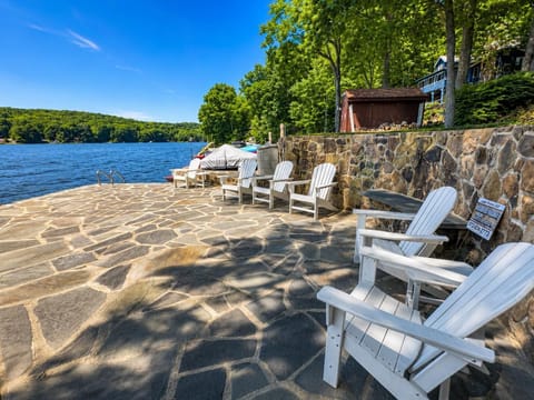 Flagstone patio with white Adirondack chairs arranged along a multi-tone stone wall overlooking the lake.