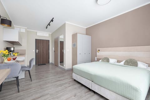 A modern studio bedroom with a king-size bed, neutral tones, and natural light from a window. The space is clean and inviting, ideal for relaxation.