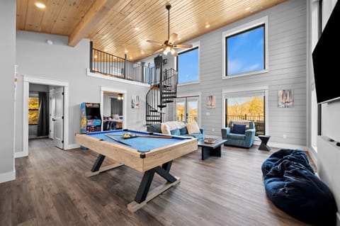 Open-concept living and game room with soaring ceilings, pool table, cozy seating, and spiral staircase. Designed for connection, this space is ideal for game nights, movie marathons, and spending quality time together.