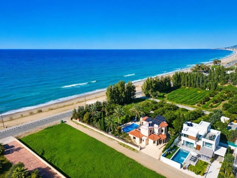 Aerial beachfront view with beautiful villas, private pools, and stunning coastline scenery.