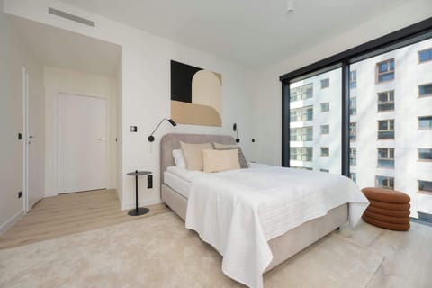 A bright bedroom with a king-size bed and large windows allowing natural light to flood the space. A mirrored wardrobe and neutral decor create a serene atmosphere.