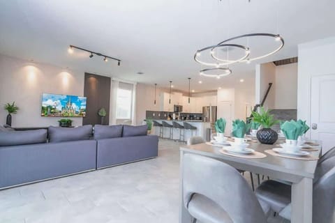 Spacious open-concept living area with a large gray sectional, stylish dining table with elegant décor, and a contemporary chandelier for a welcoming atmosphere.