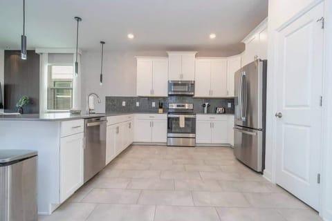 Modern, sleek white kitchen with stainless steel appliances, ample counter space, and stylish gray tile backsplash for a contemporary look.