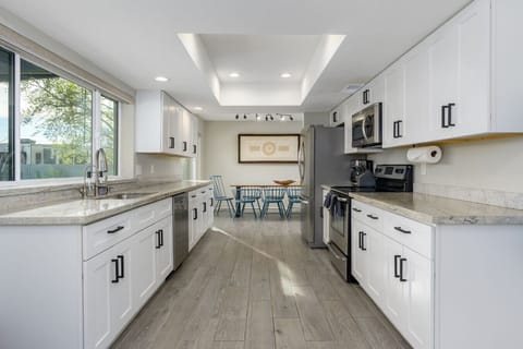 Contemporary kitchen with sleek white cabinetry, granite countertops, and stainless steel appliances opening to a stylish dining area with bold blue seating.