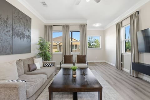 Bright, modern living room with comfy seating, smart TV, and sun-filled windows. Relax around the coffee table, enjoy open space for groups, and unwind in a calm, stylish setting—perfect for movie nights or morning coffee.
