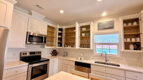 Kitchen is fully stocked with nice dishware that is white, glass, or aqua.