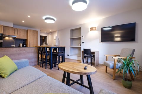 The bright living area features a comfortable sofa bed, dining table, and TV, creating a welcoming space to relax together.