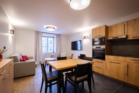 The modern living area features a cosy sofa bed, dining space, and TV alongside the fully equipped kitchen, creating a bright and comfortable place to relax.