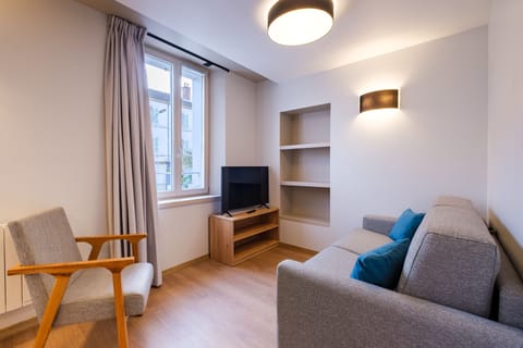 The bright living area features a cosy sofa bed, a stylish TV stand, and soft accent pillows, perfect for relaxing or unwinding.