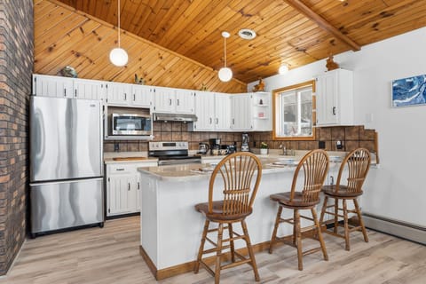 Fully equipped kitchen with stainless steel appliances, breakfast bar seating, and warm wood ceilings—perfect for cooking and gathering.