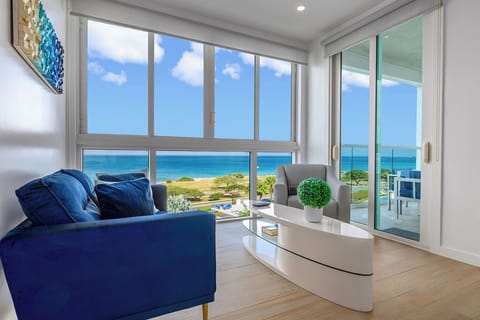 Sink into plush blue seating as ocean waves dance beyond floor-to-ceiling windows, creating your perfect seaside sanctuary.