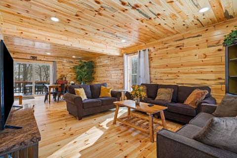Settle into the cabin living room with plush sofas, a big screen TV, and wooded views beyond the deck