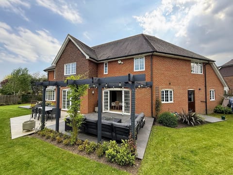 Brick house exterior with lawn, patio seating, and a pergola structure in the garden.