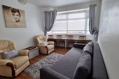 The living and dining area showing a grey sofa, two armchairs, a dining table with chairs, and a curtained window.