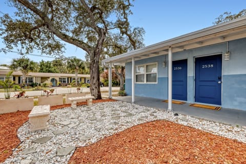 Front entrance with two doors, a gravel walkway, and landscaped plants beneath shady trees.