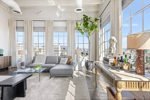 Step into comfort: sun-drenched living space with high ceilings, plush seating, and city views.