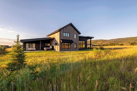 Antelope Abode at golden hour — dark modern siding, mountain peaks, and open Idaho fields as far as you can see.