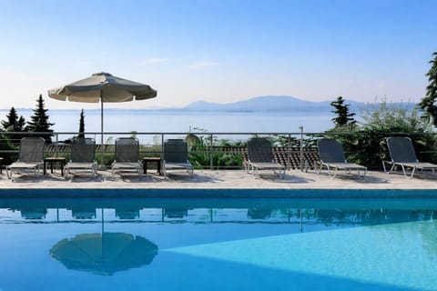 Stunning outdoor swimming pool overlooking the Ionian Sea, surrounded by sun loungers and umbrellas — the perfect place to relax and enjoy the warm Corfu sunshine.