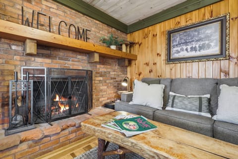 Cozy up by the stone fireplace in the warm, wood-paneled living room