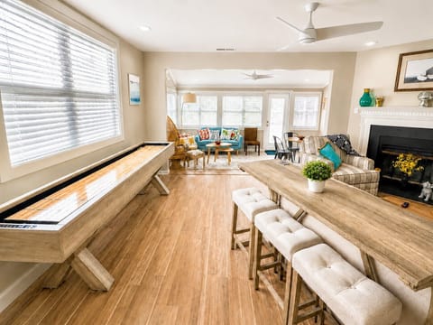 Open-concept living room with 9’ shuffleboard table, bar seating & fireplace.