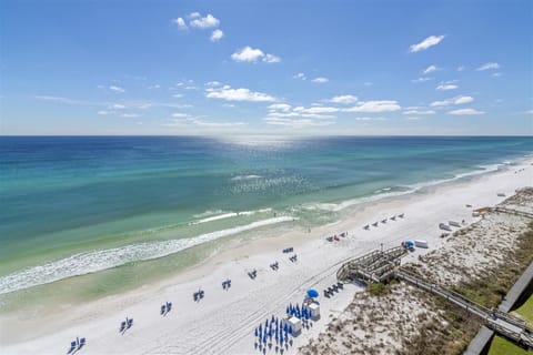 Stunning aerial view of pristine white sand beach with turquoise waters and beachside amenities including umbrellas and boardwalk access.