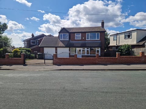 Red-brick detached house with a tiled roof, metal railings, and a front garden photographed under a clear blue sky.