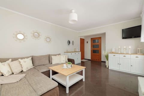 A spacious living room features a large, comfortable corner sofa in a neutral tone, complemented by a wooden coffee table and white minimalist cabinetry.