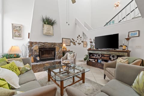 Unwind in your spacious living room where natural stone fireplace warmth meets modern comfort beneath soaring ceilings.