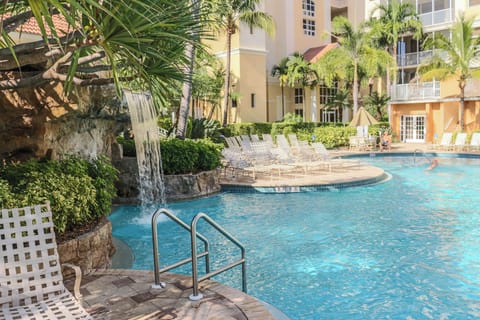 Tropical paradise awaits with a stunning waterfall cascading into crystal-clear waters surrounded by swaying palms and comfortable lounge chairs.