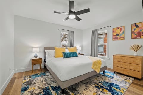 Sunny master bedroom with king bed, modern ceiling fan, and cheerful pops of color.